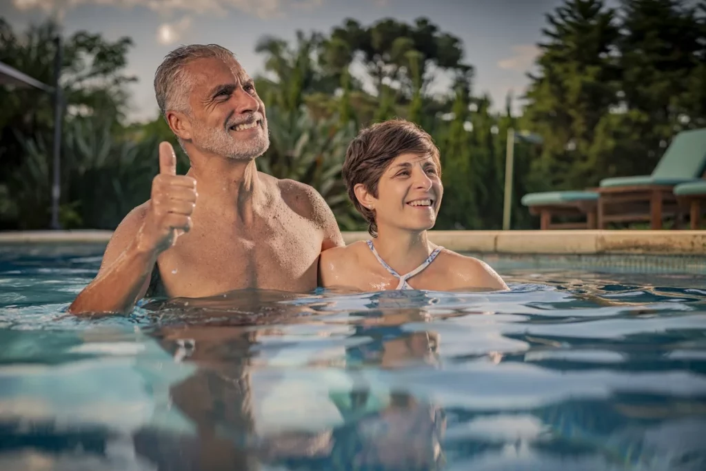 Casal feliz na piscina ao ar livre em dia ensolarado com homem fazendo sinal de positivo