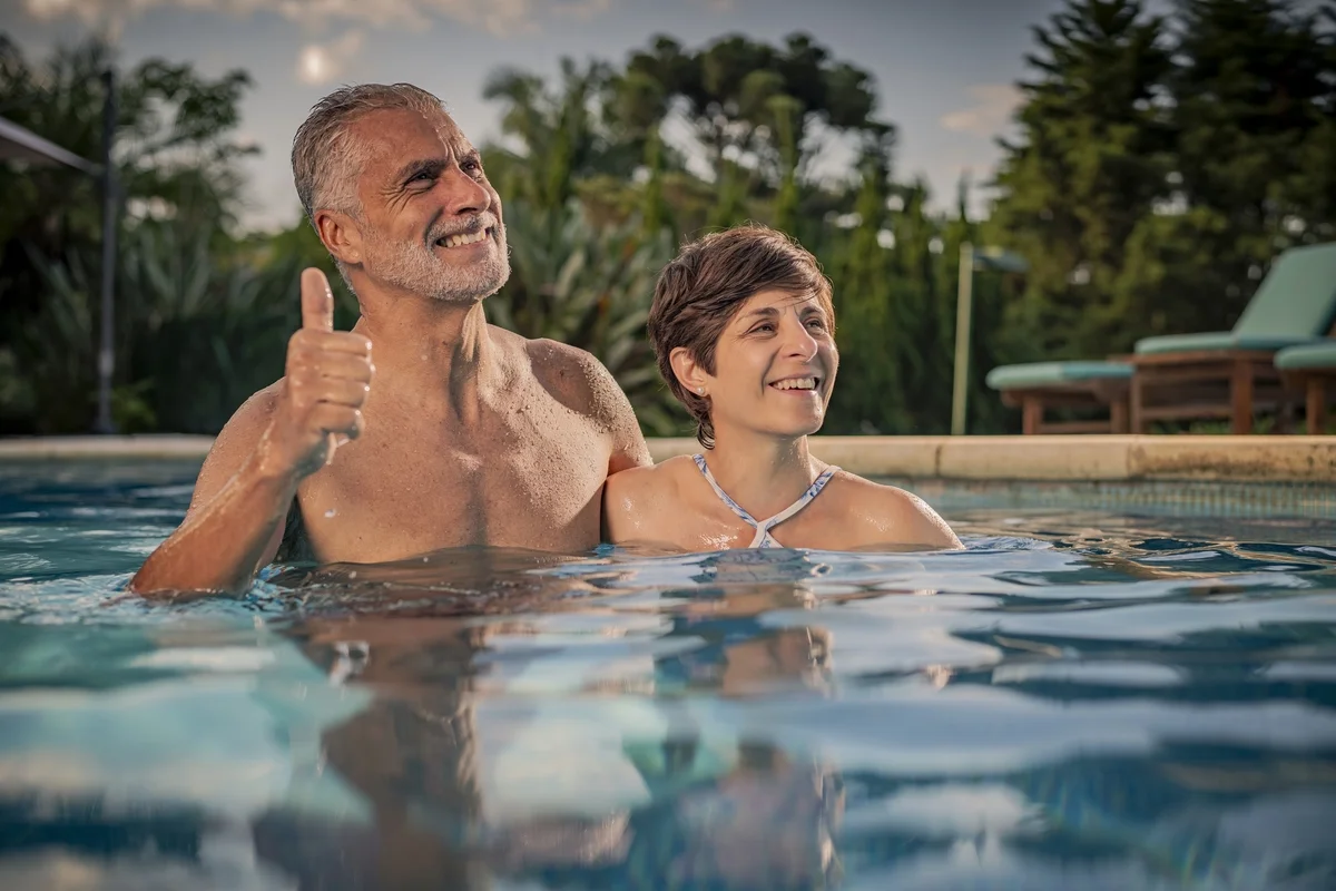 Casal feliz na piscina ao ar livre em dia ensolarado com homem fazendo sinal de positivo