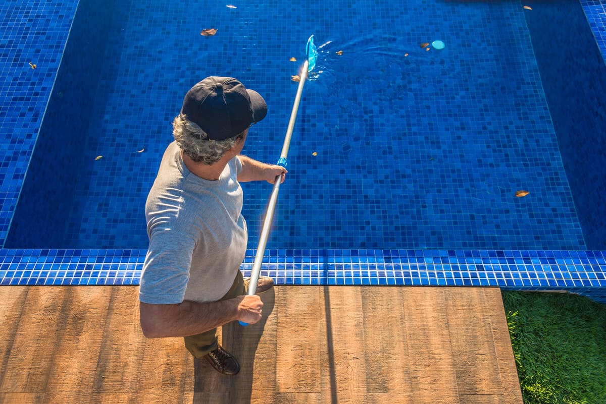 Homem limpando piscina com peneira