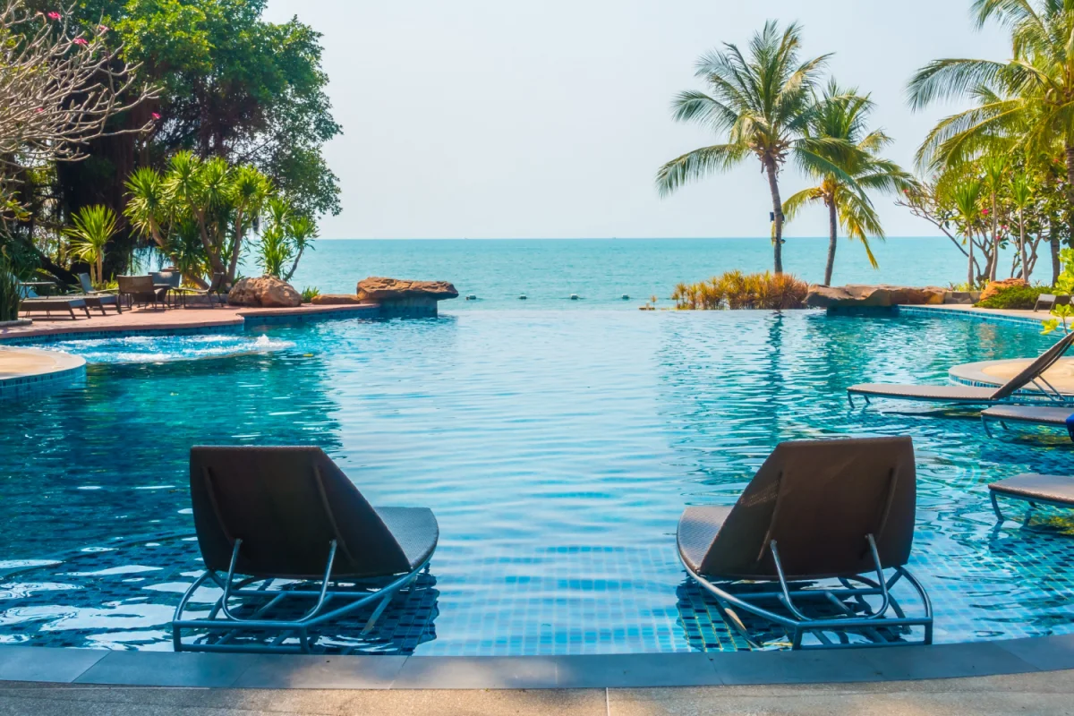 Piscina de borda infinita com espreguiçadeiras dentro da água e vista para o mar com palmeiras e vegetação tropical