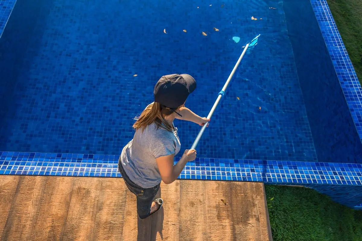 Mulher passando peneira em água de piscina