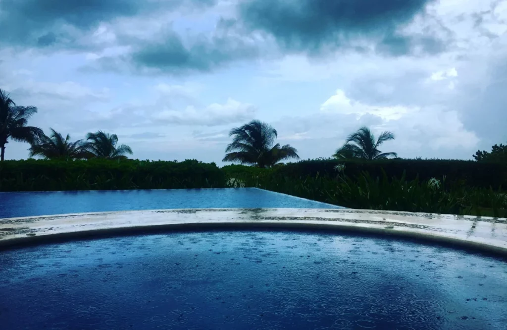 Piscina com borda branca sob céu nublado e palmeiras ao fundo