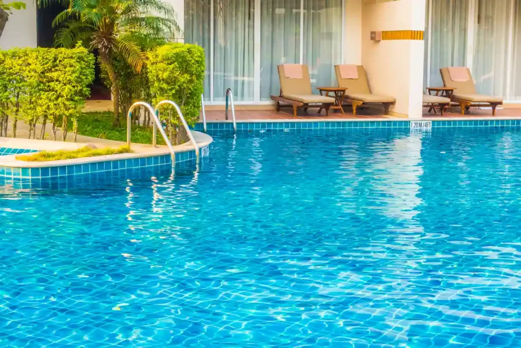 Piscina com espreguiçadeiras e área de lazer cercada por plantas verdes.