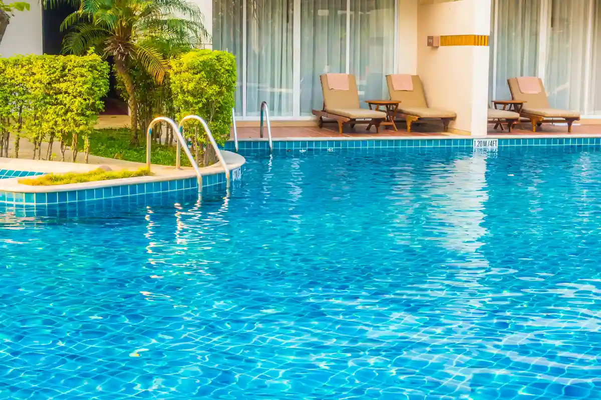 Piscina com espreguiçadeiras e área de lazer cercada por plantas verdes.