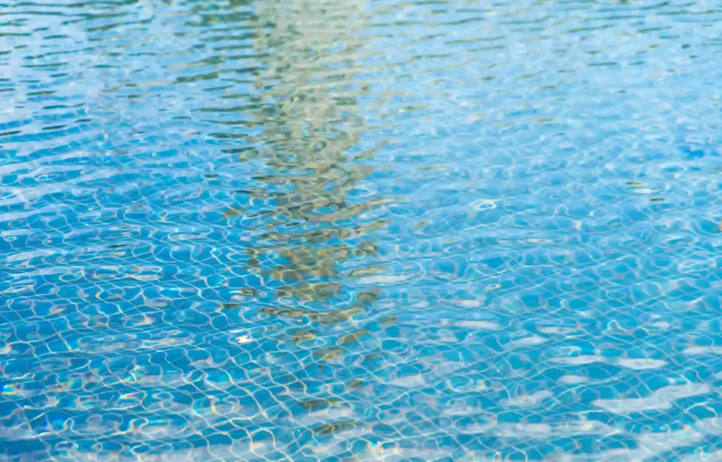 Vista de uma piscina com água azul clara e efeito de ondulação nas últimas luzes do dia, refletindo o céu ao redor.