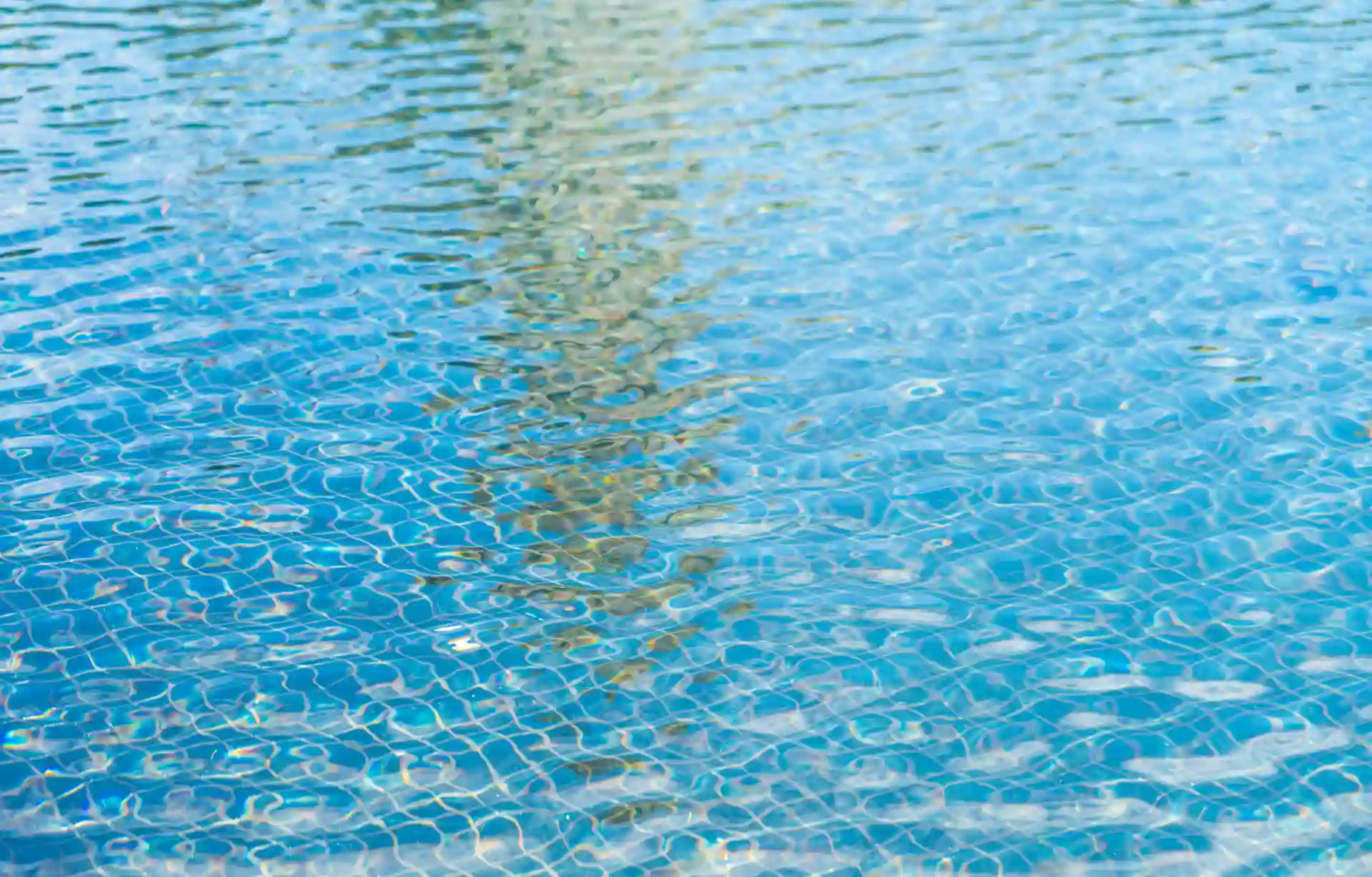 Vista de uma piscina com água azul clara e efeito de ondulação nas últimas luzes do dia, refletindo o céu ao redor.
