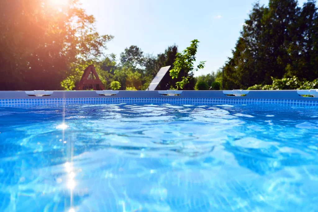 Piscina exterior azul con agua cristalina que refleja el sol en un día soleado con árboles al fondo
